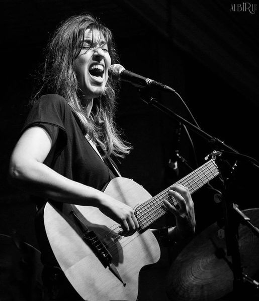 Susana Raya passionately singing and playing guitar during a performance