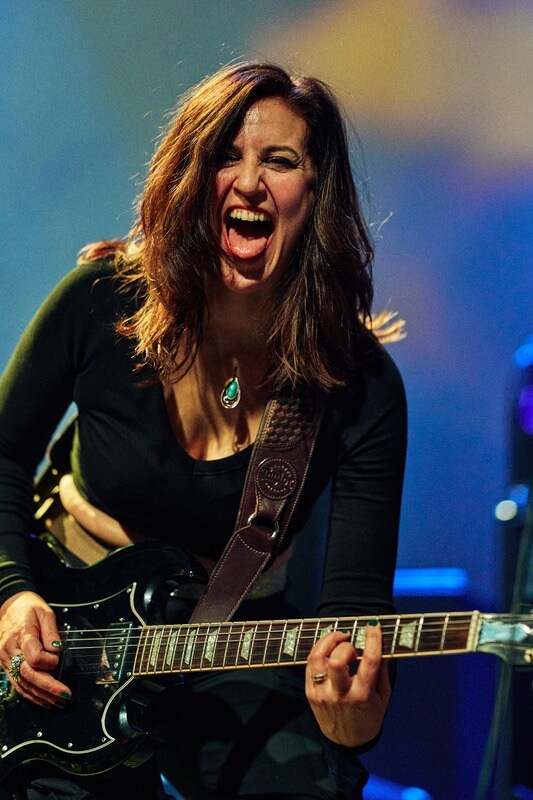 Susana Raya rocking out on stage with a black Gibson SG standard guitar, exuding energy and passion.