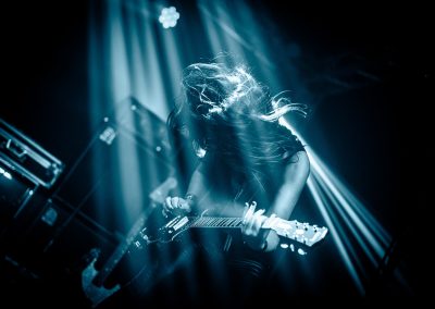 Susana Raya, the Spanish member of Inhalo, with long hair plays an electric guitar on stage, with dramatic lighting and motion blur emphasizing her energy. Susana Raya playing with Dutch progressive Rock band Inhalo