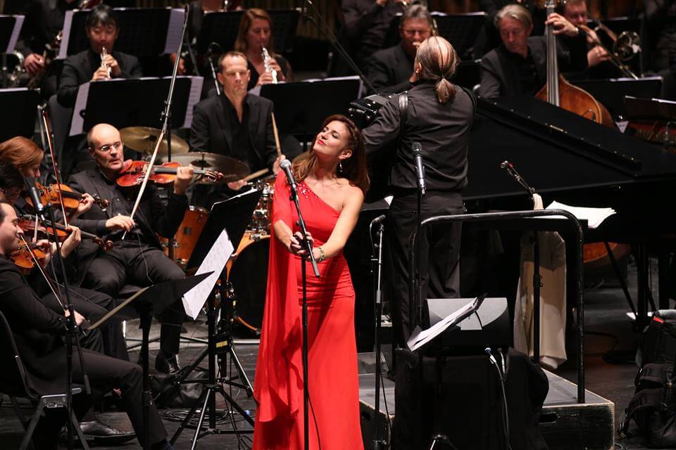 Spanish jazz singer Susana Raya in a vibrant red dress singing on stage alongside the WDR Symphony Orchestra of Cologne